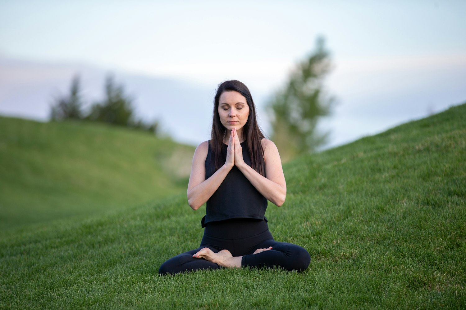 Mom sitting quietly on a grassy hill at dusk, eyes closed, finding calm