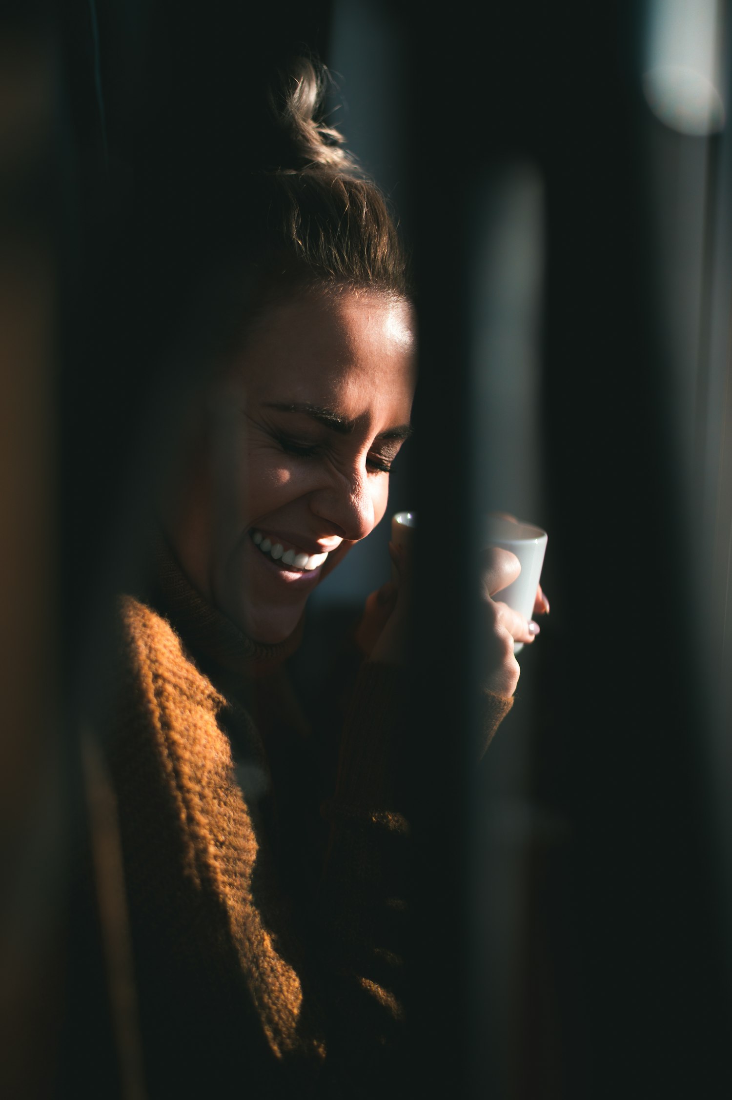 A mom laughing with a warm mug as morning light spills across her