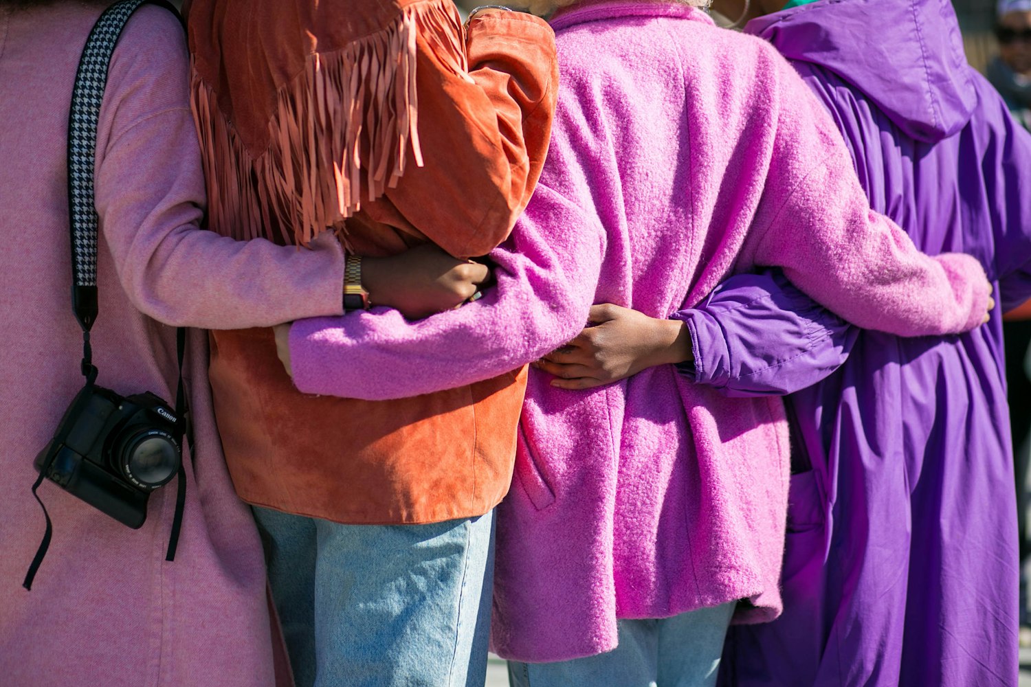 A group of women in bright coats with their arms wrapped around each other
