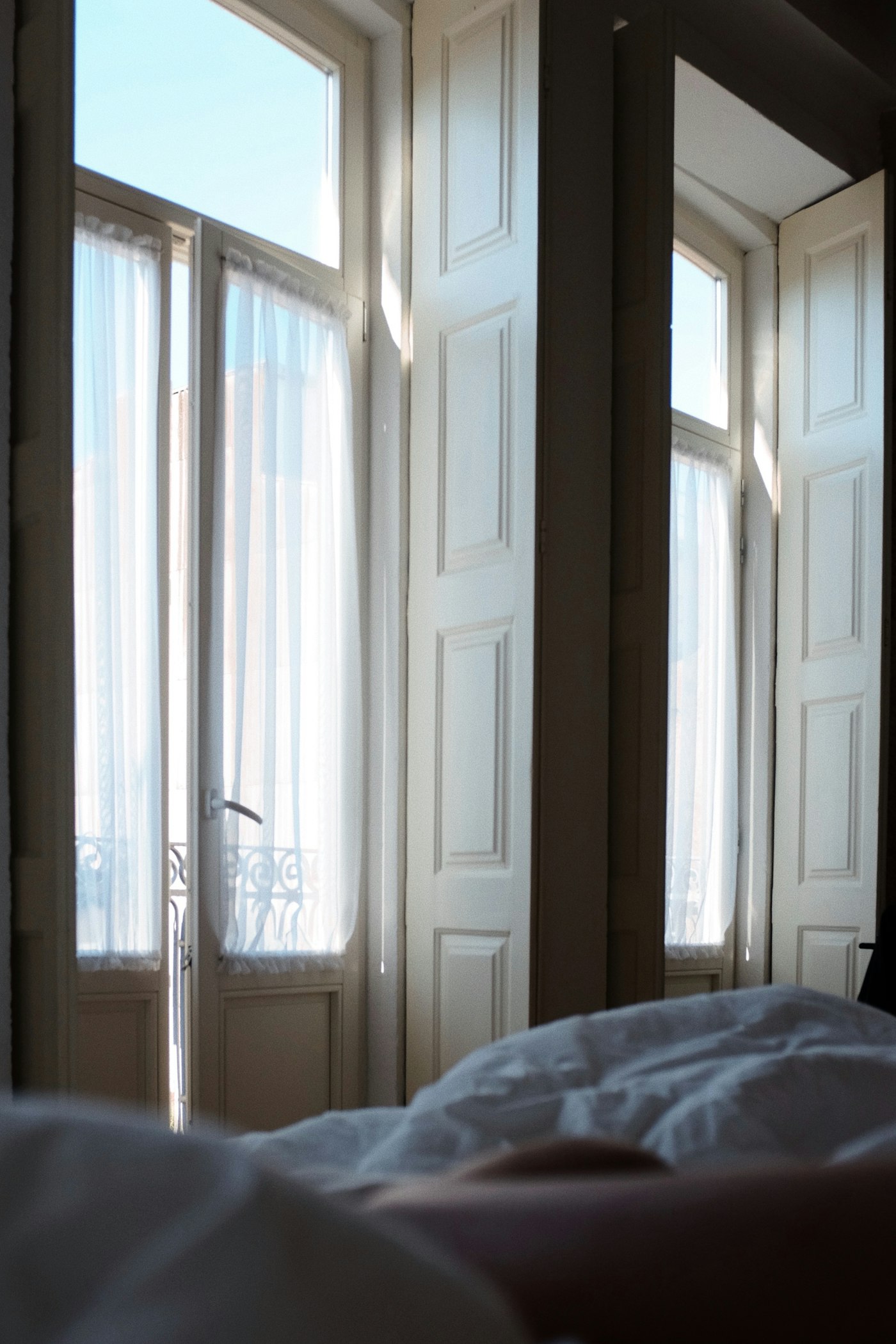 Soft morning light pouring through tall windows over an unmade bed