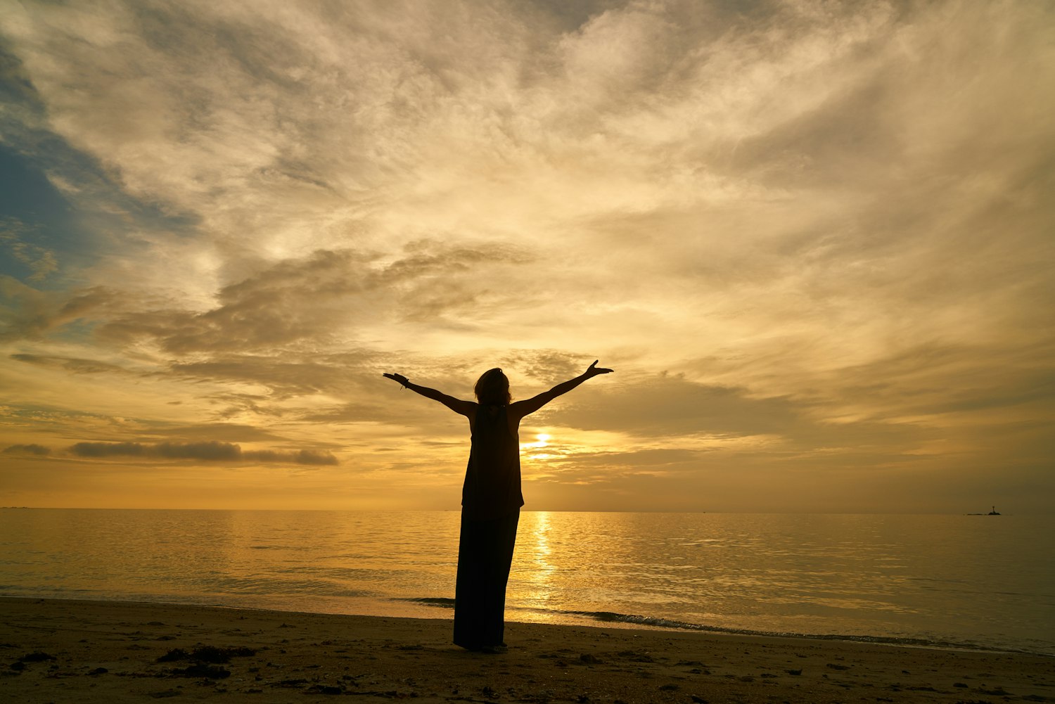 A woman standing on the shore at sunrise with her arms thrown open to the sky