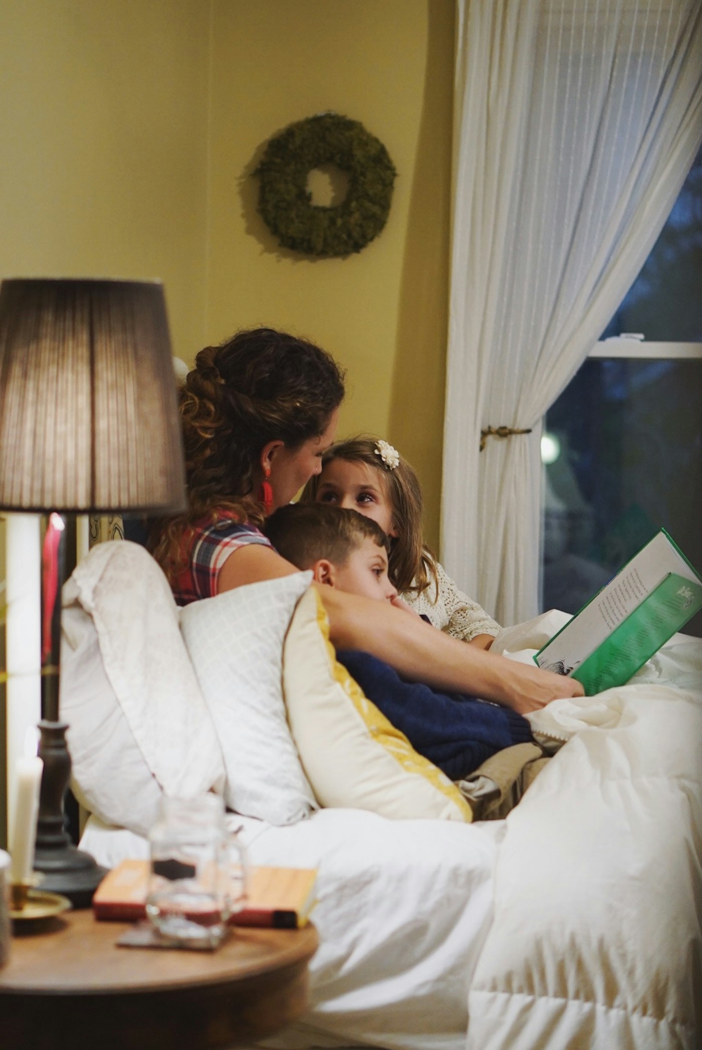 Mother reading a book to her two children by warm lamplight