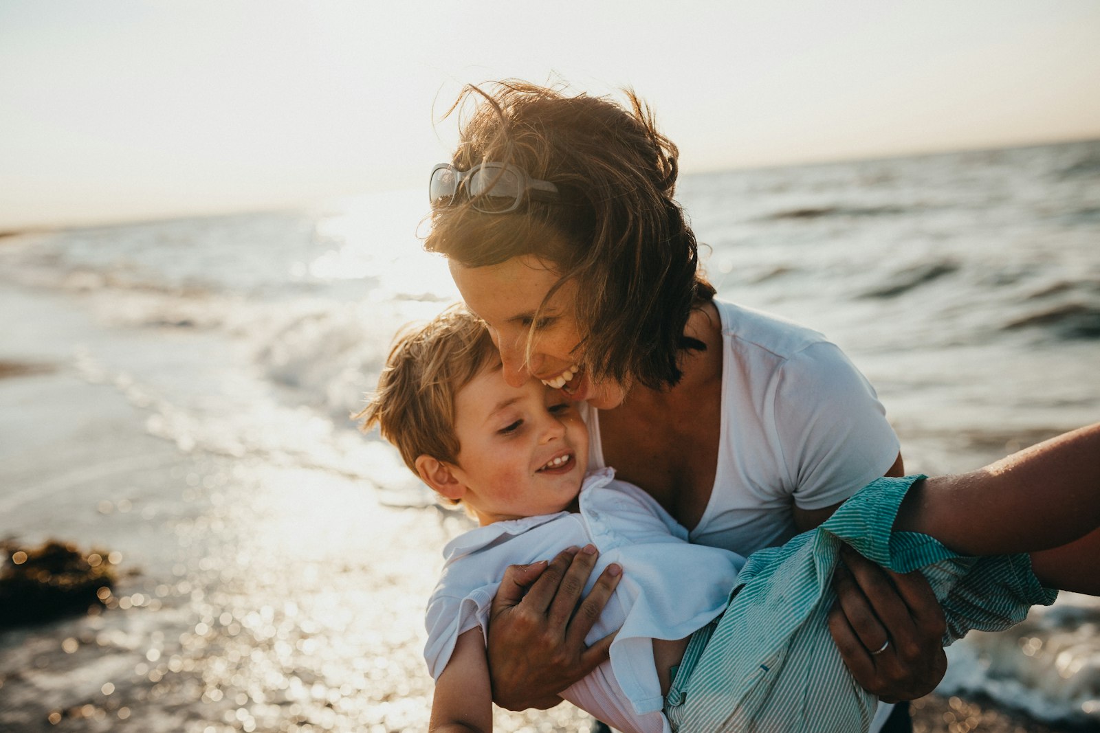 Mother laughing and embracing her young son on the beach at golden hour